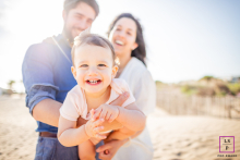 A Heartfelt Family Portrait in Hérault In Hérault, a heartwarming family photograph showcases parents happily presenting their laughing baby in the foreground, with their faces beaming with pride and joy against a beautiful natural backdrop.