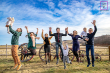 Boundless Joy: A Family's Leap in the Heart of Hérault In Hérault, a family captures a moment of pure joy as they all leap into the air simultaneously, against a backdrop of lush greenery and clear blue skies, their expressions filled with laughter and excitement.