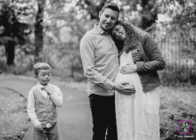 Dans la Loire, un jeune garçon ajuste joyeusement sa tenue, après s'être habillé pour une séance photo, tandis que ses parents se tiennent à proximité, le père berçant le ventre de sa femme enceinte