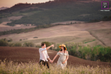 In Val d'Orcia, Tuscany, a maternity portrait features expectant parents walking through a field surrounded by rolling hills. The stunning landscape complements the serenity and joy of this special time.