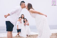 Boston Toddler Shines Amid Parental Embrace, Captured in a Heartfelt Portrait of Family Love In Boston, Massachusetts, a toddler is the center of attention, lovingly framed by the out-of-focus profiles of their parents in the foreground.