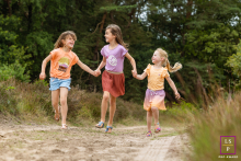 In Noord-Holland, The Netherlands, three sisters hold hands as they run joyfully along a dirt roadway.