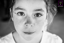 In Vanzy, Haute-Savoie, France, a tight black and white portrait captures a young girl smiling, highlighting her captivating eyes and freckles. The intimate shot reflects her natural beauty and joyful spirit.