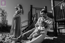 Afternoon Sun and Laughter: A Family's Happy Yarmouth Park Day. A pregnant mother watches as a dad and daughter slide down a slide together, laughing. The family is enjoying an afternoon at a park in Yarmouth, Massachusetts, USA.