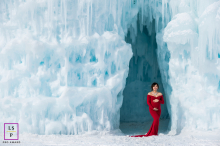 A pregnant mother stands in a red dress in New Hampshire, New England. She is surrounded by blue ice.
