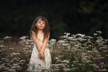 A girl is standing in a field of flowers in Portland, Oregon. She is basking in the sweet, warm glow of the setting sun. The portrait captures her youth and innocence.