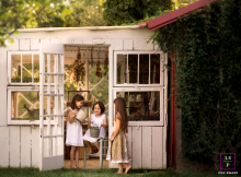 Three sisters are laughing while standing in a doorway of a greenhouse in Chattanooga, Tennessee. The scene is reminiscent of a Norman Rockwell painting.