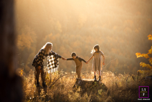 A family of three is playing follow the leader on rocks in Portland, Oregon. They are backlit by the setting sun, with a forest in the background. The portrait captures their playful interaction.