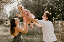 In Montpellier, a parent lifts their baby playfully into the air, both smiling with delight. The joyful interaction captures a lighthearted and fun-filled connection between parents and child.