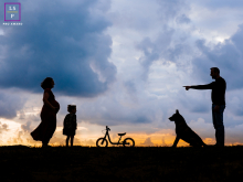 In Tarnos, Landes, a family is silhouetted against a dramatic sky. A pregnant woman stands with her partner and child, who has a bike positioned in the center of the frame, highlighting family unity.