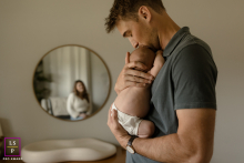 San Antonio Parents' Love Reflected in a Gentle, New Family's Embrace In San Antonio, Texas, a dad gently holds his newborn while the mother's reflection appears in a nearby mirror, capturing both parents' presence and love in a tender family scene.