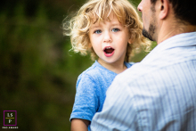 Father and Son: A Peaceful, Inquisitive Child in Cupertino, California. In Cupertino, California, a father holds his young son for a family portrait. The boy gazes at the camera with an inquisitive expression, as they are together in a peaceful outdoor setting.