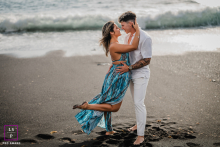 On the beach in Lanzarote, Canary Islands, a couple hugs at the shoreline. She lifts her leg playfully as wind blows her hair, capturing their joy and connection by the sea.