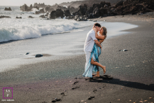 On a Lanzarote, Canary Islands beach with dark sand, a couple shares a kiss. The beachscape creates a striking backdrop, highlighting their affection against the island’s distinctive volcanic shoreline.