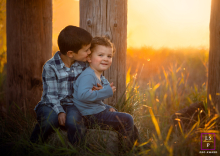 Golden Portland Light Illuminates Two Brothers Sharing a Warm Secret Beside Pilons In Portland, Oregon, an older brother leans in to tell a secret to his younger brother as they sit beside wooden pilons, backlit by golden, warm-toned light.
