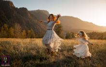 Mom And Daughter Twirl Together On Hillside In Golden Sunset Light In Portland, Oregon, mom and daughter twirl together on a hillside at sunset, backlit by golden, warm-toned light.