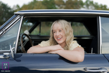 Wisconsin Girl Smiles Brightly Leaning Out Vintage Grandpa's Car Window In West Bend, Wisconsin, a teenage girl sits in the driver’s seat of her grandpa’s vintage car, leaning out the window and smiling brightly.