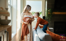Big Brother Tenderly Kisses His Newborn Sibling In Portland Home Session In Portland, Oregon, a brother gently kisses his newborn sibling on the couch during an indoor home session in the living room.