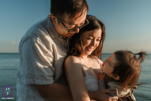 In Toronto, Ontario, a family enjoys time at the beach as mom, dad, and their toddler share affectionate smiles in soft, golden sunlight.