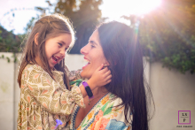 In Curitiba, Brazil, a mother embraces her child at sunset, a warm smile on her face as the sun bursts behind them.