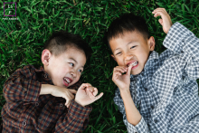 Two young brothers in Los Gatos, California, laughing joyfully while playing together on green summer grass, capturing childhood fun.