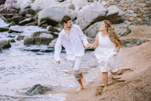 Are they outrunning the tide or just racing toward a shared future? Their intertwined hands and the woman’s gathered hem create a delightful, kinetic layer against the rugged Spanish stone.