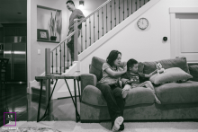 In this Oregon home, everyday family life unfolds quietly as a mother reads with her son while the father descends the stairs after bedtime duties. The black and white tones give the candid scene warmth, stillness, and honesty.