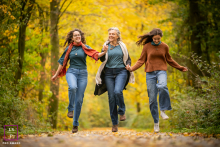 Mother And Two Daughters Hop Together Along Autumn Path In Delft A mother and her two daughters hold hands while playfully hopping together along an autumn woodland path in Delft, the Netherlands.