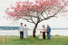 A multigenerational family gathers beneath a blooming cherry blossom tree beside the waterfront during a spring lifestyle session in Seattle.