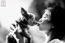 Mountain View, California Love: A Woman and Her Dog A black-and-white pet portrait shows a woman in Mountain View, California, kissing a small dog. The photo is a profile shot, taken outdoors.