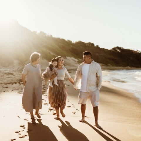 This lifestyle portrait captures an enchanting sunset beach session in Sydney with a joyful family and their grandmother, radiating happiness in the warm sunlight