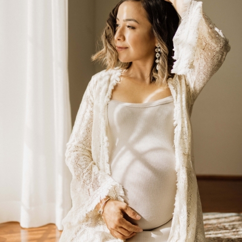 This stunning lifestyle portrait captures a mother's serene beauty as she sits solo on wood floors in her white dress, with a backdrop of natural light pouring in from a window in Sydney, New South Wales