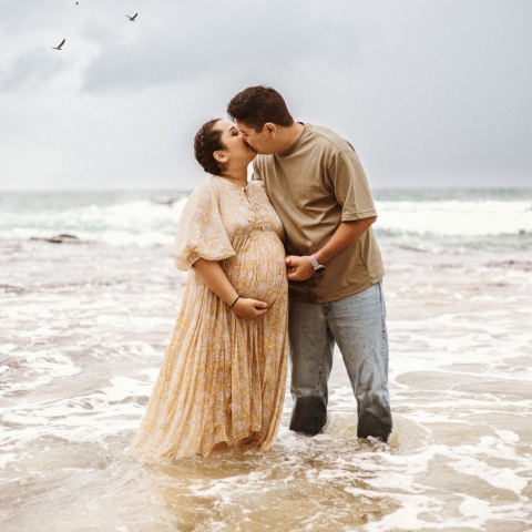 This breathtaking lifestyle portrait captures a couple knee deep in crashing surf during a sunrise maternity beach session in Sydney, New South Wales